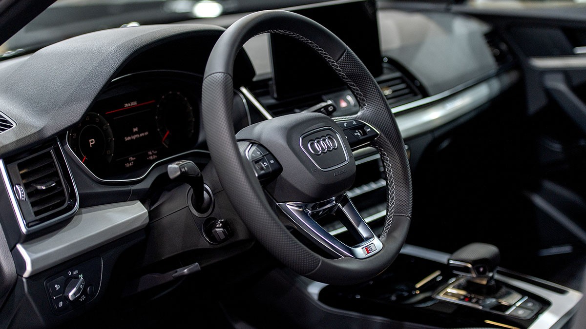 Close-up of an Audi car interior showing the steering wheel, digital dashboard, and gear shift in a sleek, modern design.