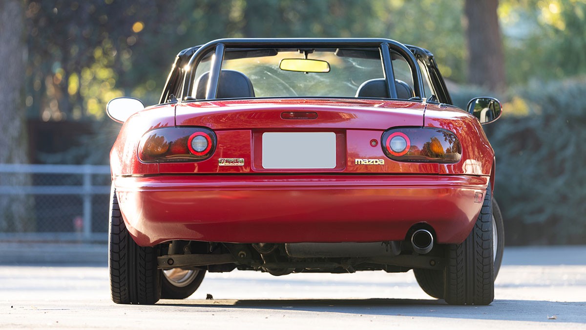 Rear view of a red convertible sports car parked outdoors, with visible taillights and a single exhaust pipe.