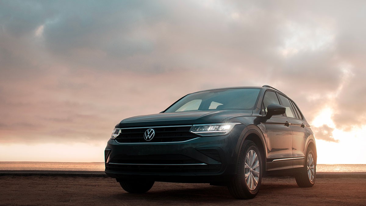 A black SUV parked on a coastal road at sunset, with a cloudy sky and the ocean in the background.