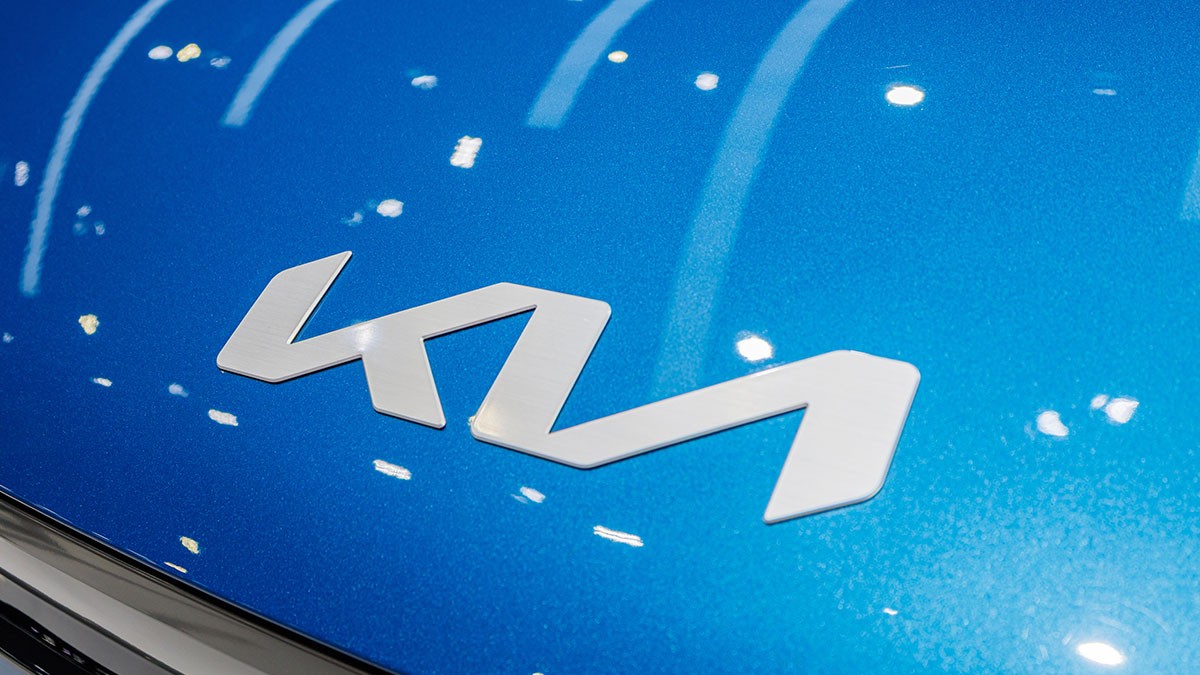 Close-up of a silver "Kia" logo on a shiny blue car hood with reflections of overhead lights.