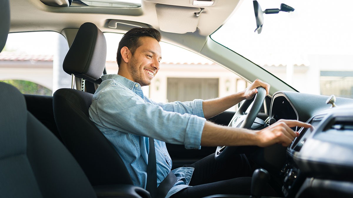 Man smiling while adjusting the car stereo, sitting in the driver's seat of a parked vehicle.