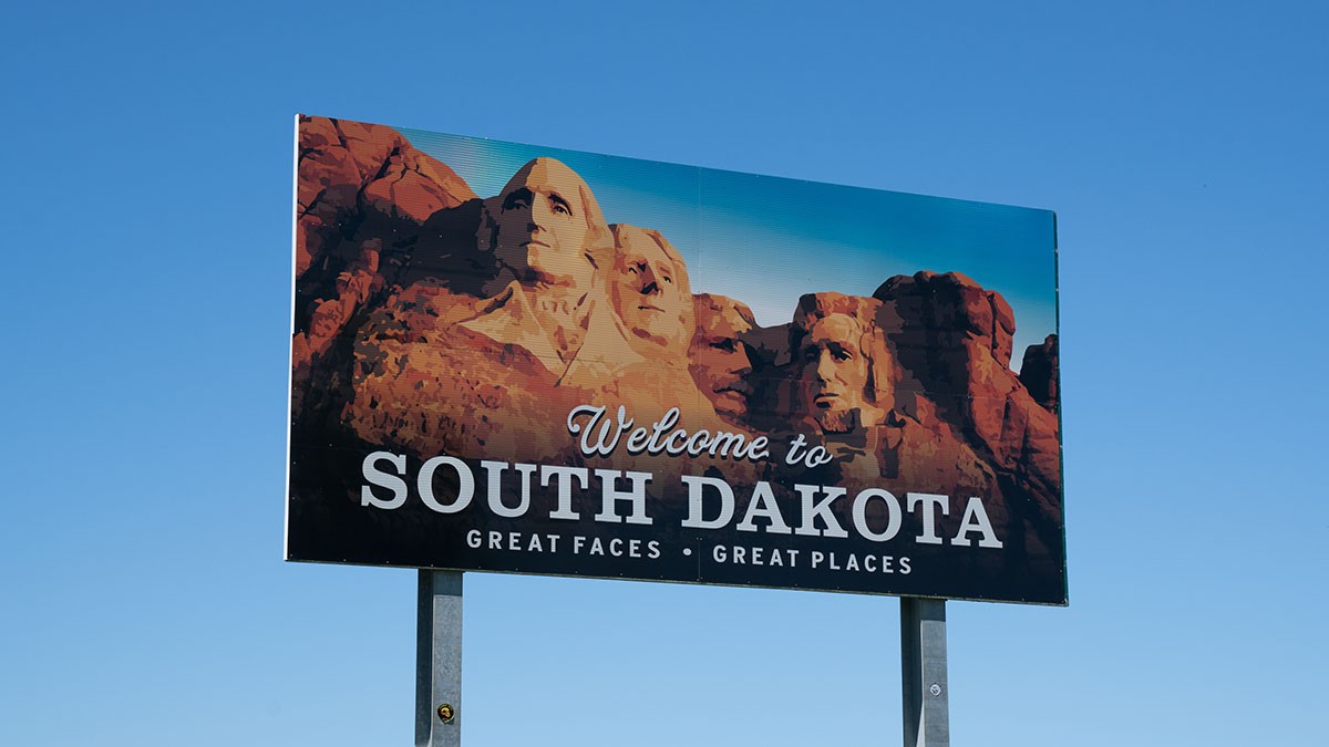 Billboard with Mount Rushmore and text "Welcome to South Dakota, Great Faces, Great Places" against a clear blue sky.