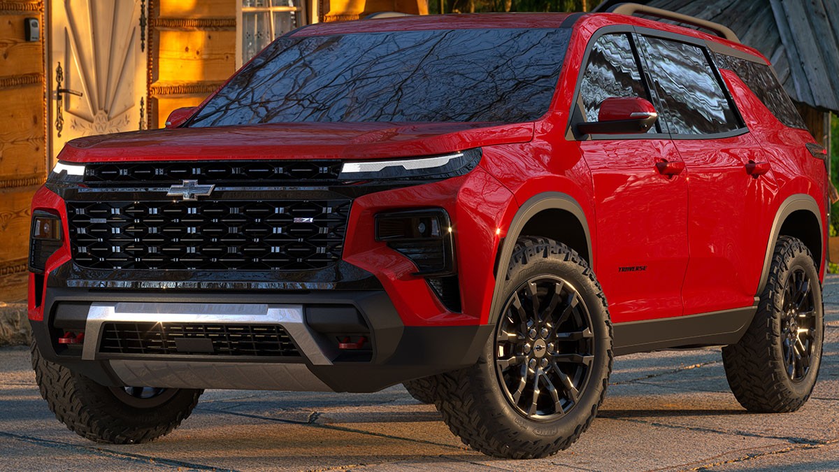 A red SUV with rugged tires and a sleek design is parked outdoors, reflecting trees on its windows.