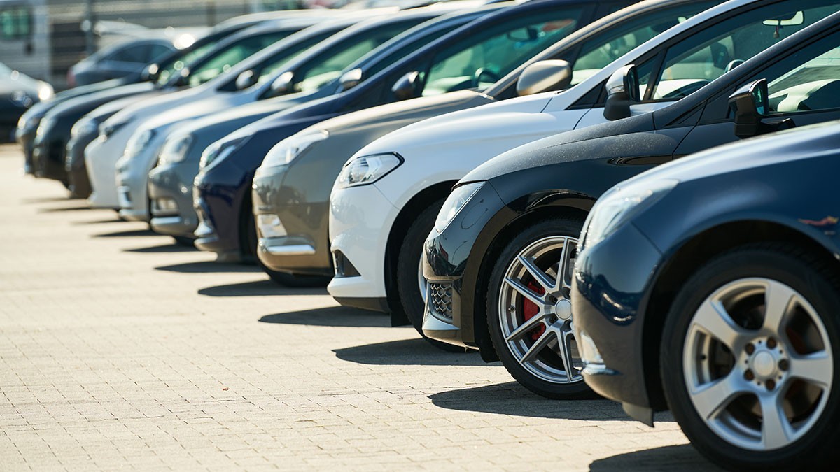 A row of parked cars of various colors and makes, aligned neatly in a parking lot on a sunny day.