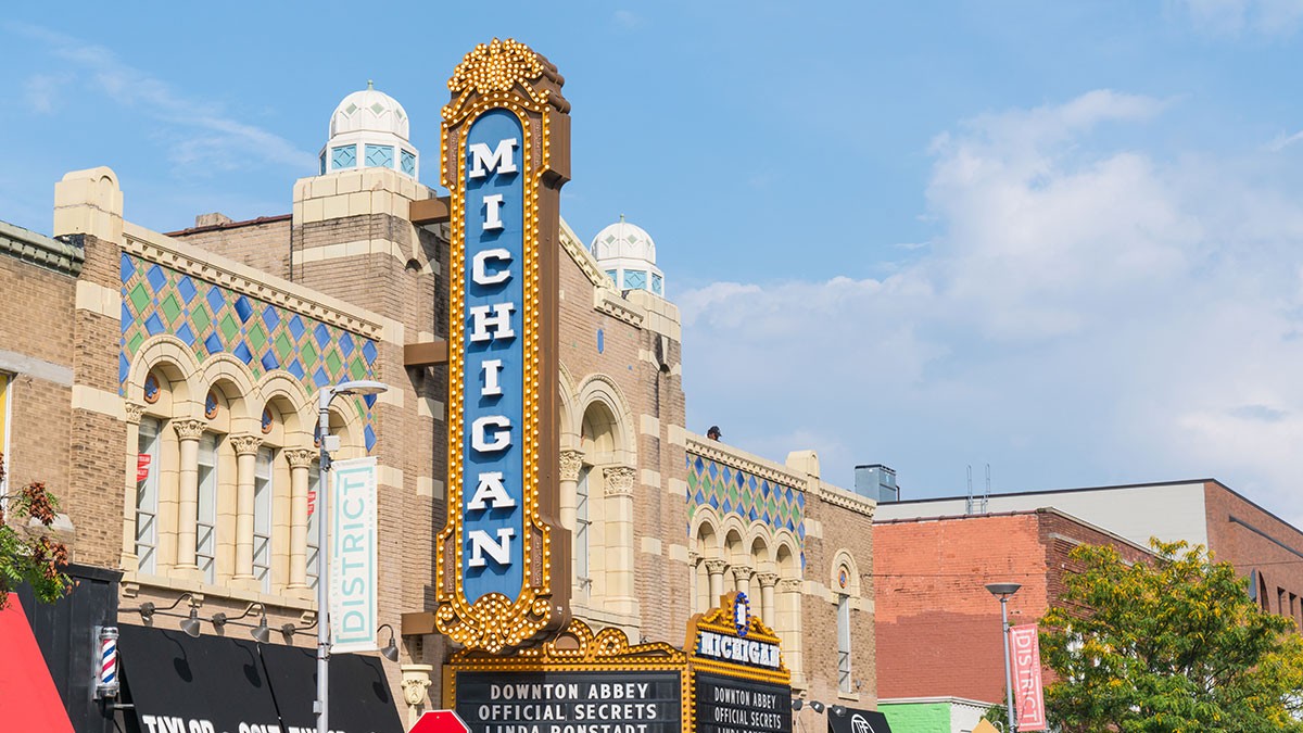 Historic theater with a marquee reading "Michigan," featuring ornate architecture and colorful detailing against a blue sky.