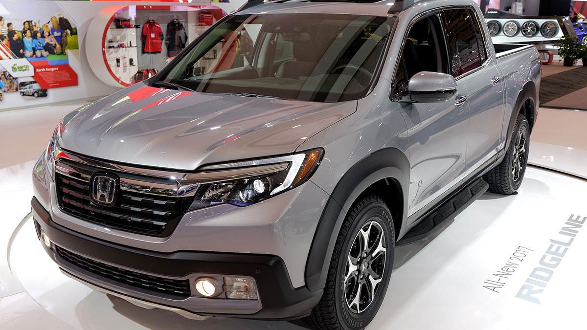 Silver Honda Ridgeline pickup truck displayed in a showroom with bright lighting and automotive accessories in the background.
