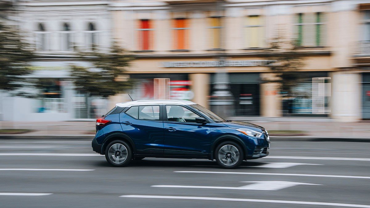 Blue SUV driving on a city street with blurred buildings in the background, conveying motion.