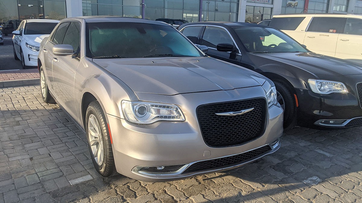 Silver Chrysler 300 sedan, front three-quarter view, parked on a paved lot beside a dark sedan.