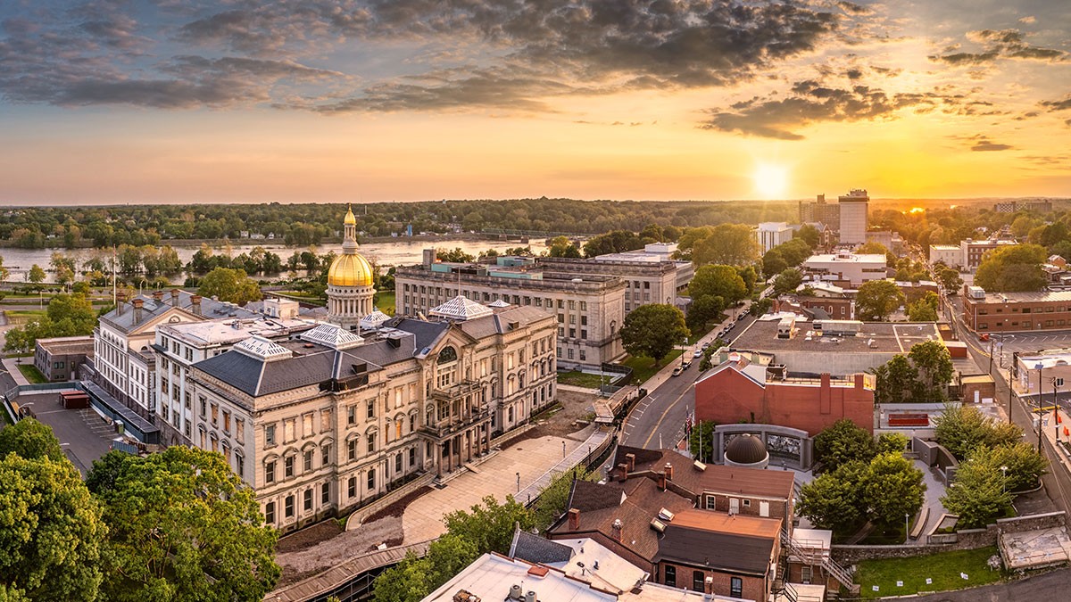 Aerial view of a cityscape at sunset with a prominent building featuring a golden dome, surrounded by trees and urban structures.