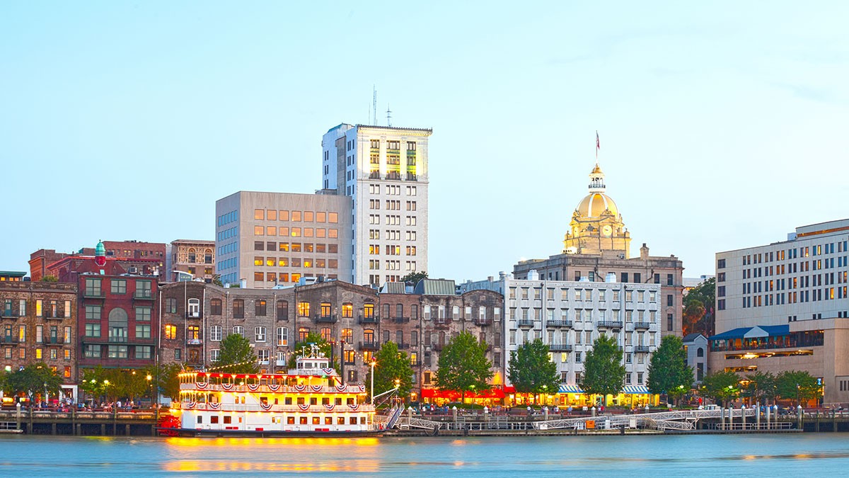 A riverboat sails on a river with a backdrop of historic buildings and a golden-domed structure under a clear sky.