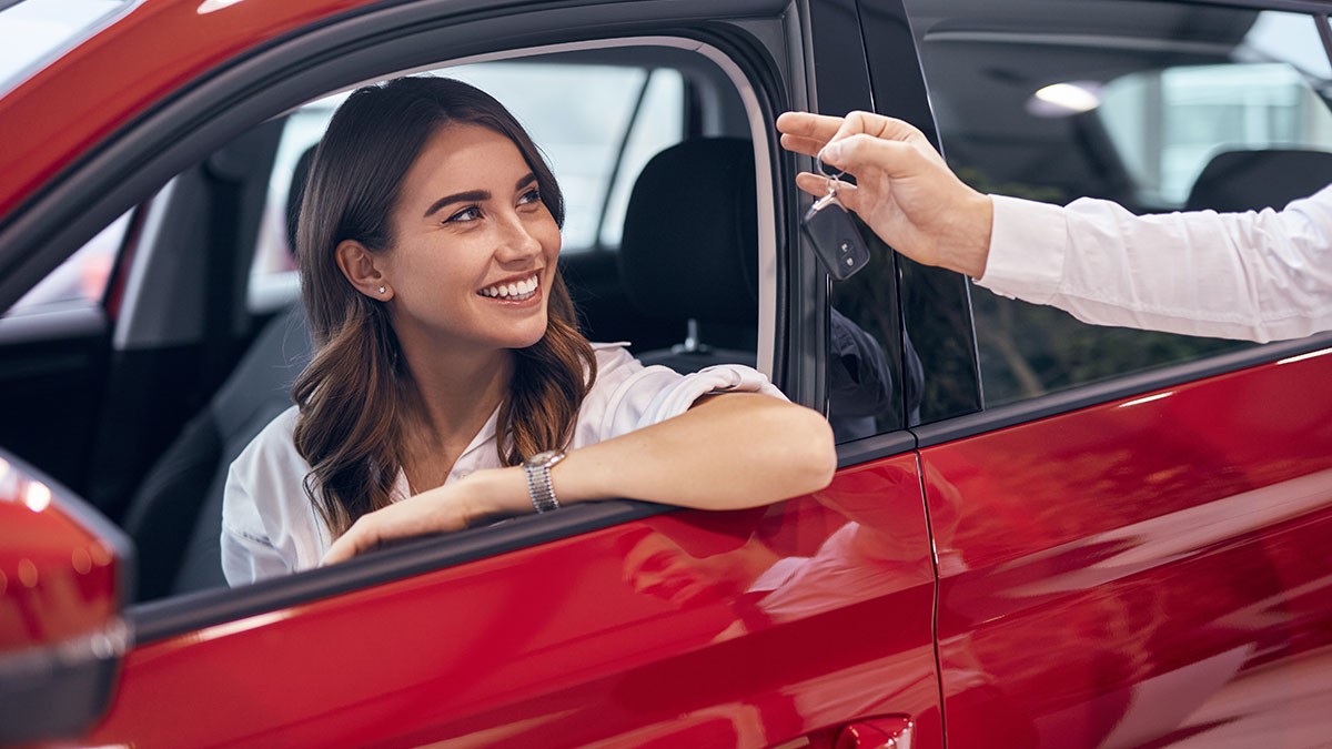 Woman in a red car smiles as a person hands her car keys through the window.
