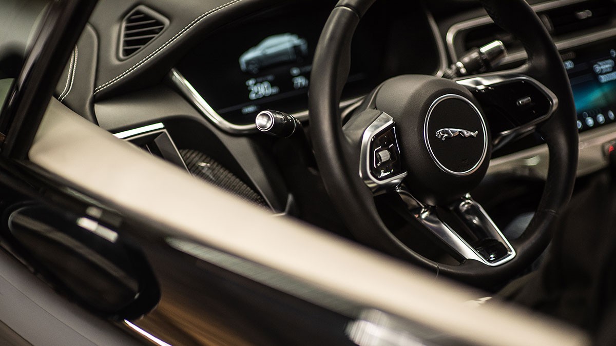 Close-up of a car interior showing a sleek steering wheel with a logo, digital dashboard, and modern design elements in a dimly lit setting.