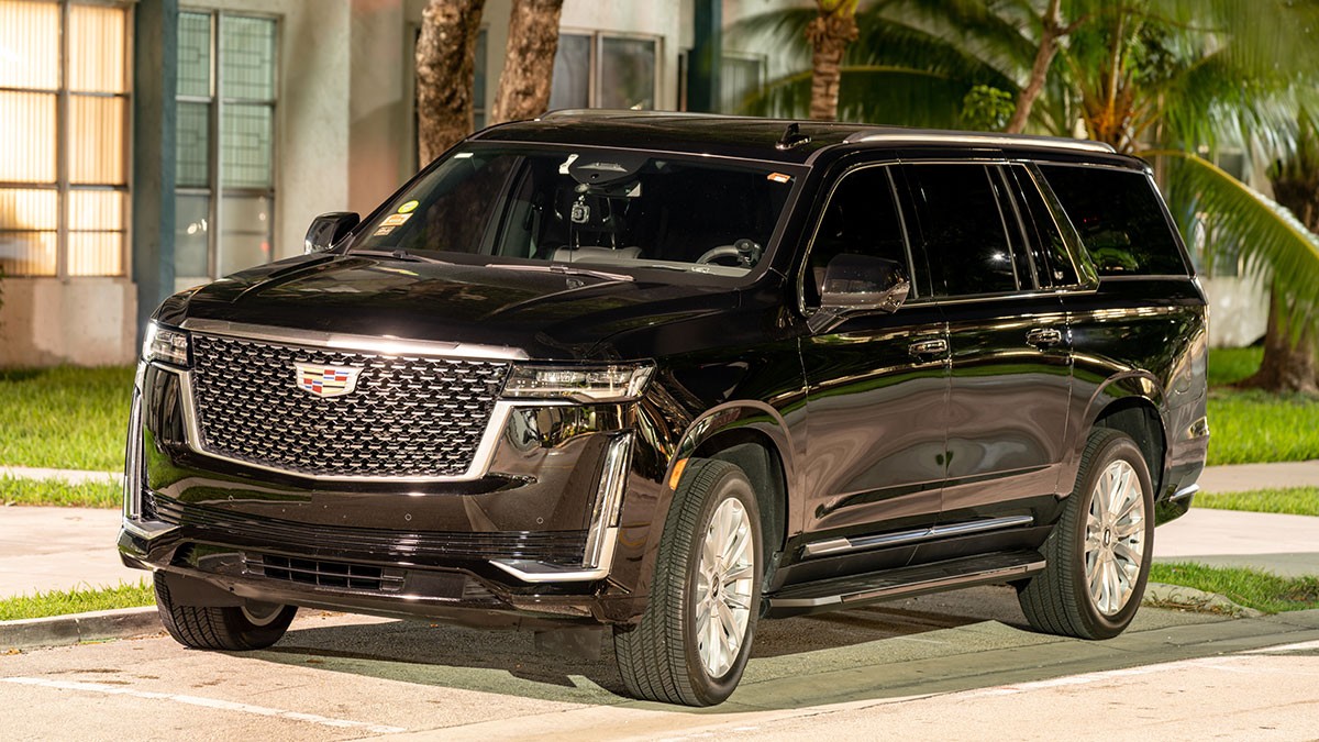 A black SUV parked on a street at night, featuring a large grille and chrome accents, with a building and palm trees in the background.