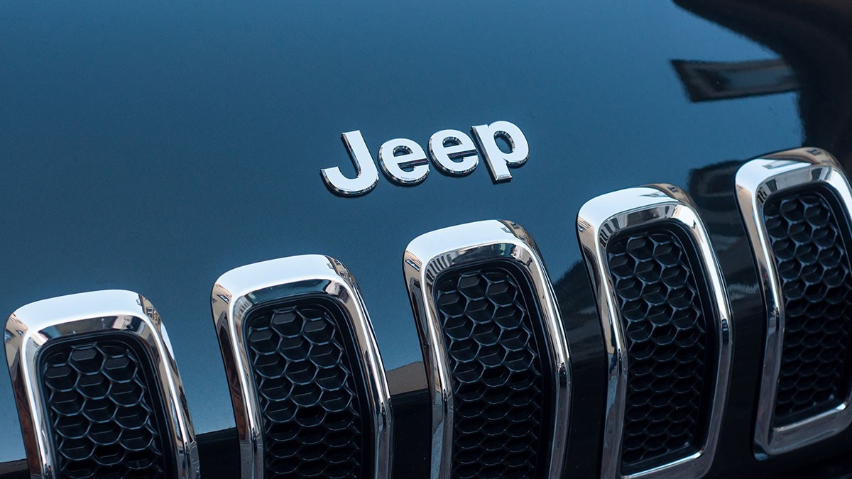 Close-up of a Jeep car grille, featuring the brand logo above the chrome-trimmed, black honeycomb-patterned vents.