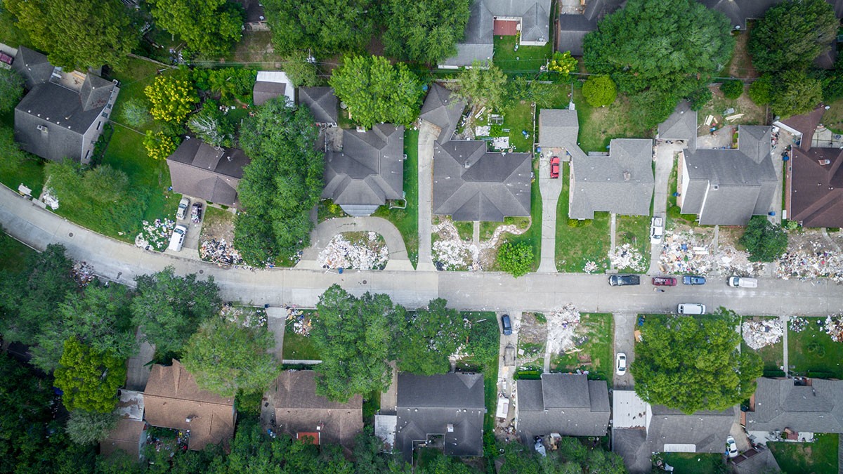 Aerial view of a neighborhood with houses, trees, and debris on the lawns, indicating possible storm damage.