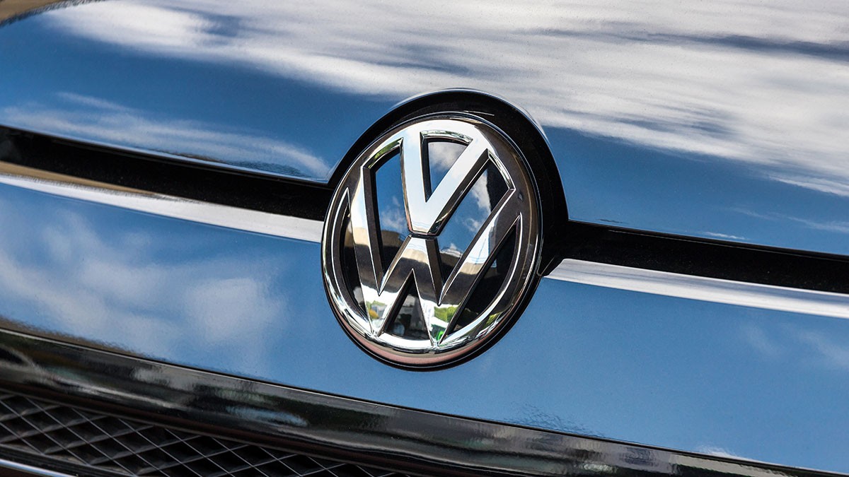 Close-up of a Volkswagen logo on a car grille, reflecting blue sky and clouds.