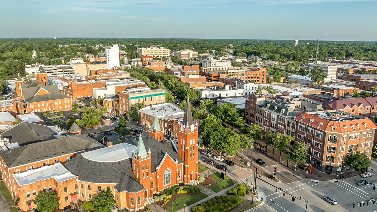 Aerial view of a small city's downtown with a red brick church with twin spires, surrounding buildings and tree-lined streets