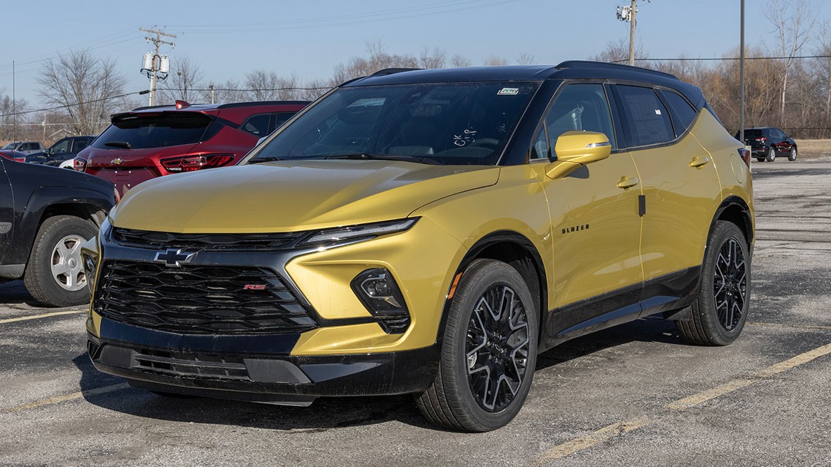Gold Chevrolet SUV parked in a lot, featuring black accents, sleek headlights, and large black wheels under a clear sky.