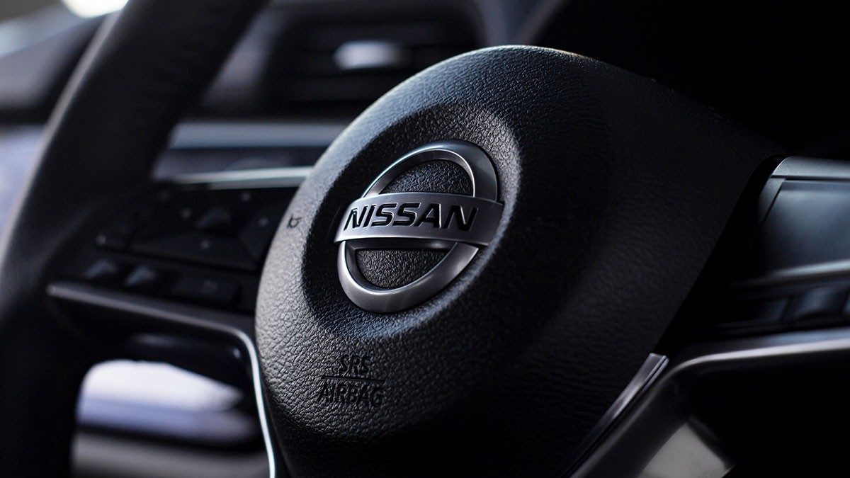 Close-up of a Nissan steering wheel, showcasing the logo and textured surface, with dashboard details blurred in the background.