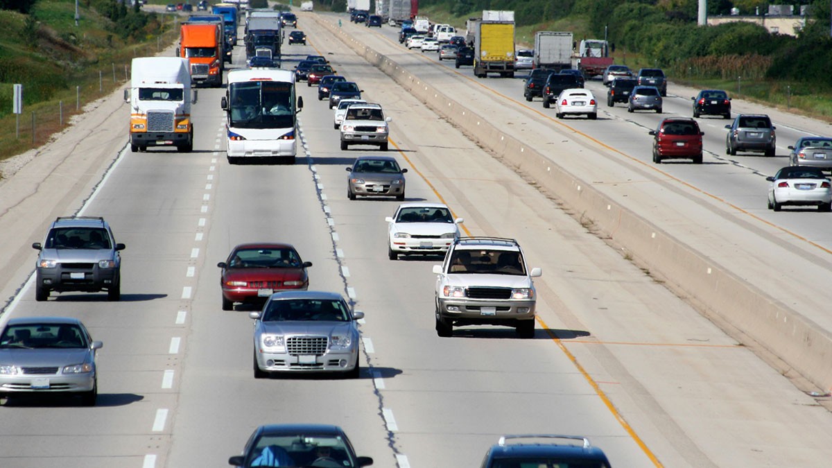 A busy multi-lane highway with various vehicles, including cars, trucks, and a bus, traveling in both directions under a clear sky.
