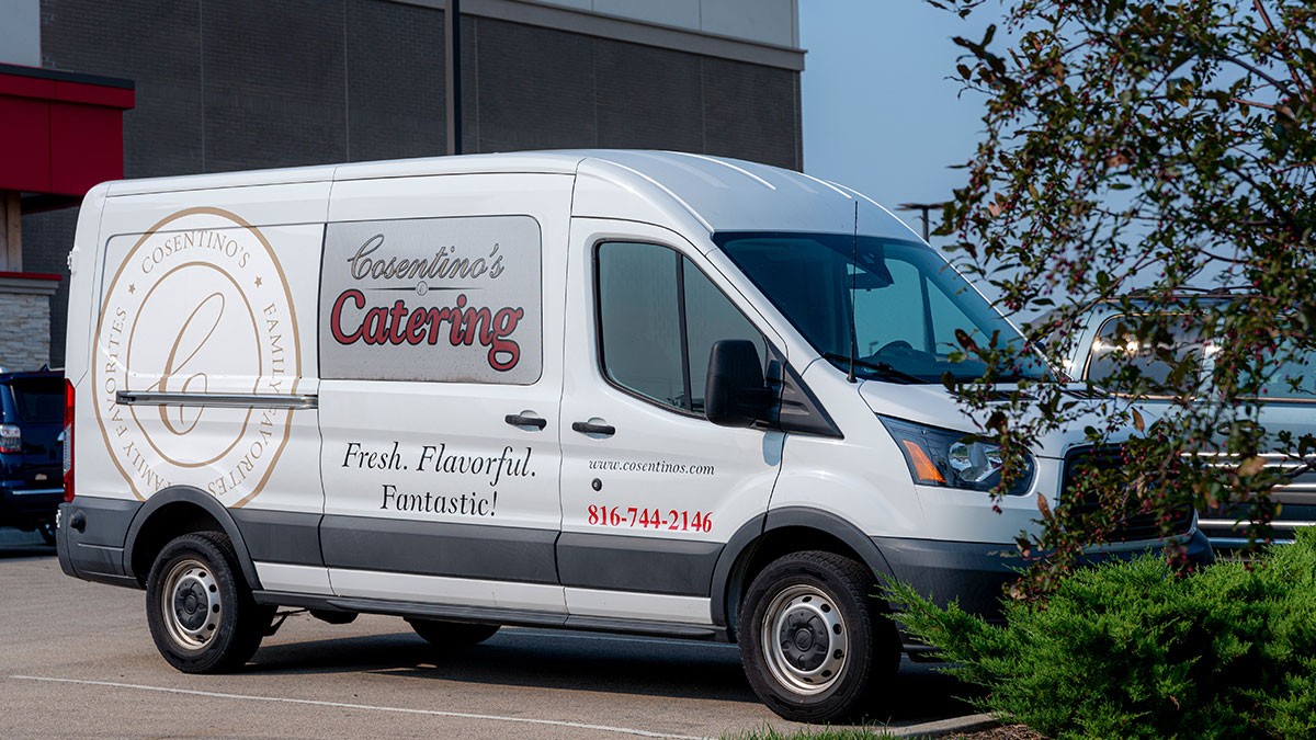 White catering van parked in a lot, featuring "Cosentino's Catering" logo and contact details on the side.