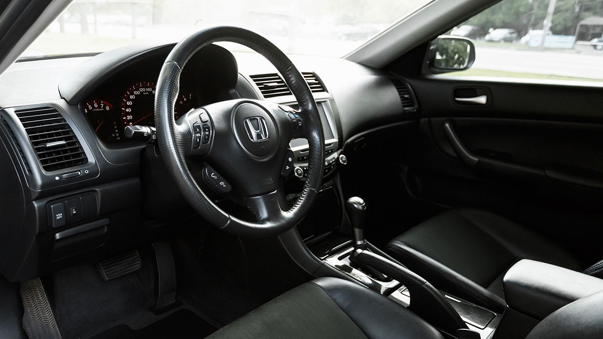 Interior of a car showing the dashboard, steering wheel with a logo, gear shift in neutral, and black leather seats.