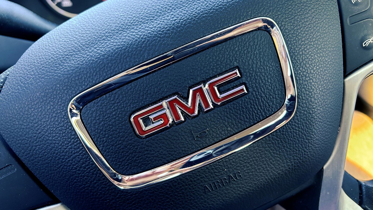 Close-up of a GMC steering wheel, featuring the red GMC logo on a textured black surface with chrome accents.