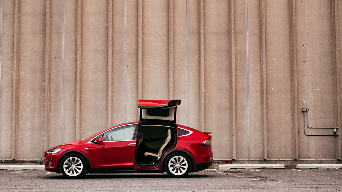 A red car with its rear passenger door open, parked in front of a large concrete wall.