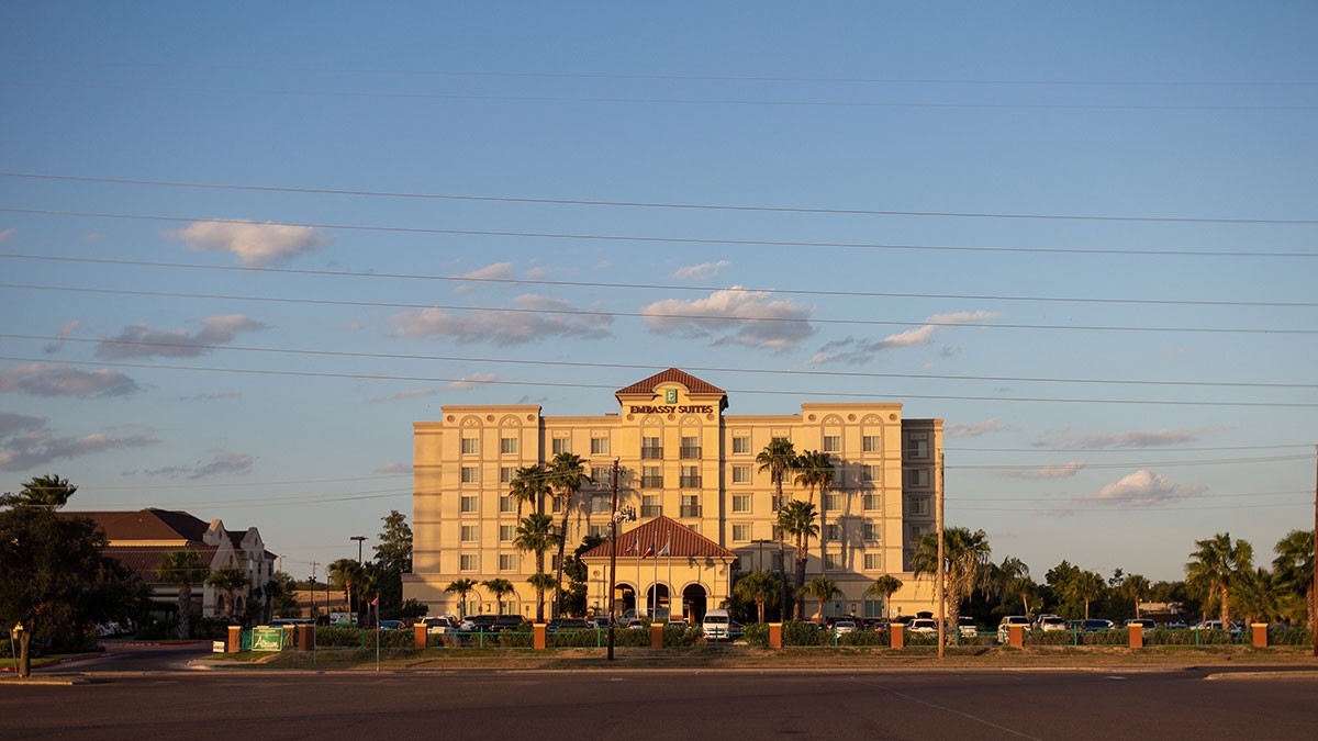 Hotel building with palm trees in front, under a clear blue sky with a few clouds.