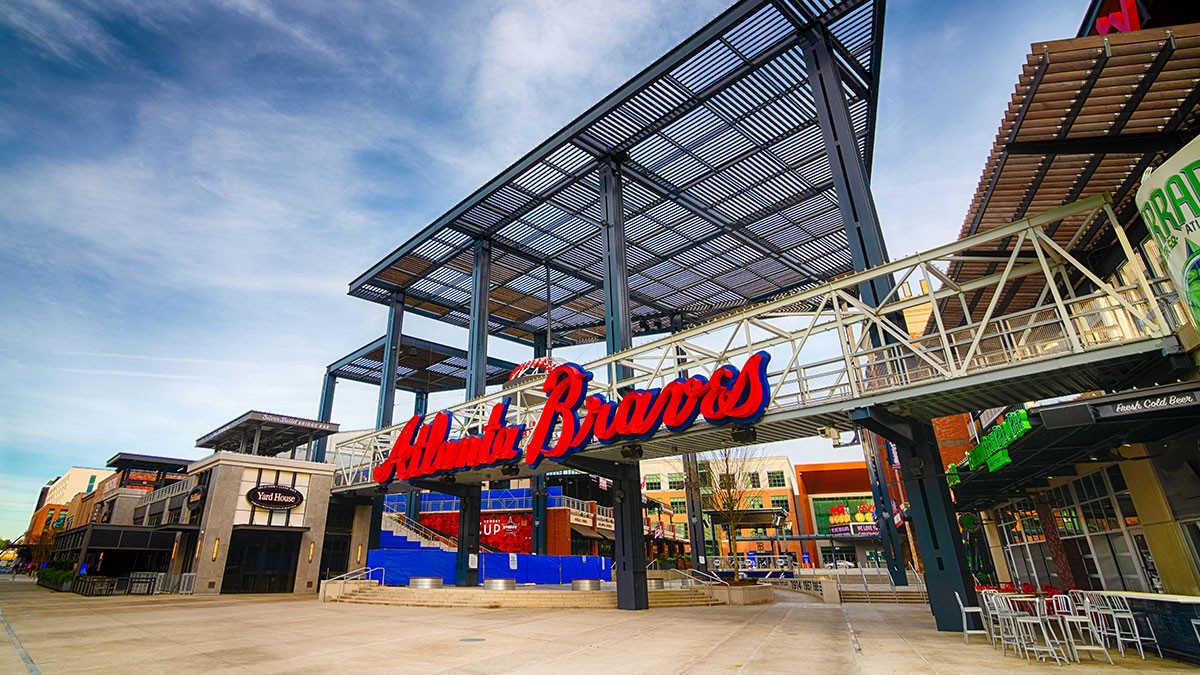 Entrance to a modern baseball stadium with "Atlanta Braves" in bold red letters, featuring open steel structures and surrounding shops.