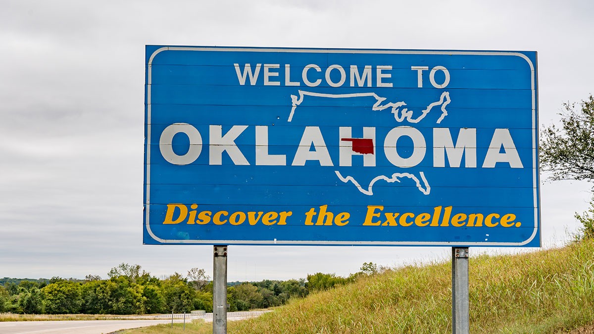 Welcome sign for Oklahoma on a roadside, featuring a map of the U.S. outline and the phrase "Discover the Excellence."