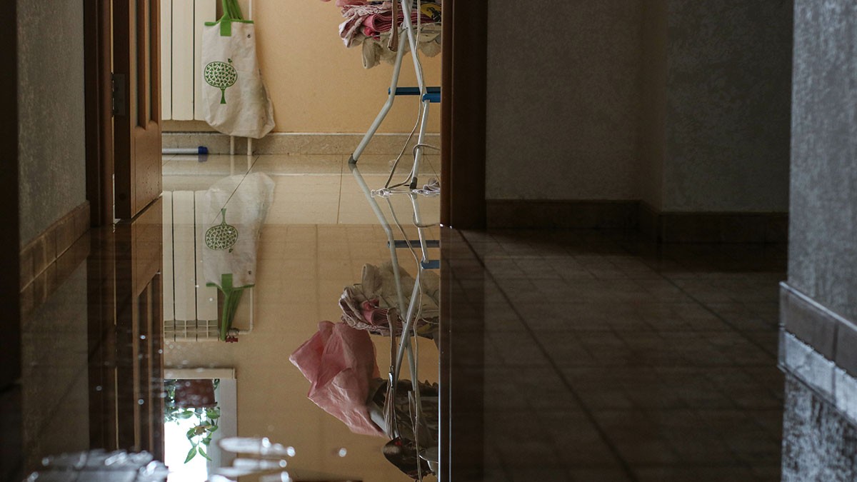 A hallway with tiled floor is partially flooded, reflecting a clothes drying rack and a door leading to another room.