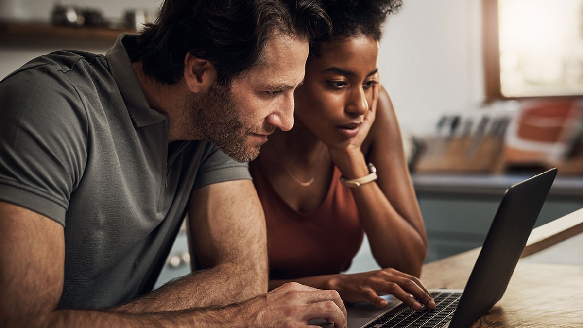 A man and woman intently look at a laptop screen together in a cozy, well-lit room.