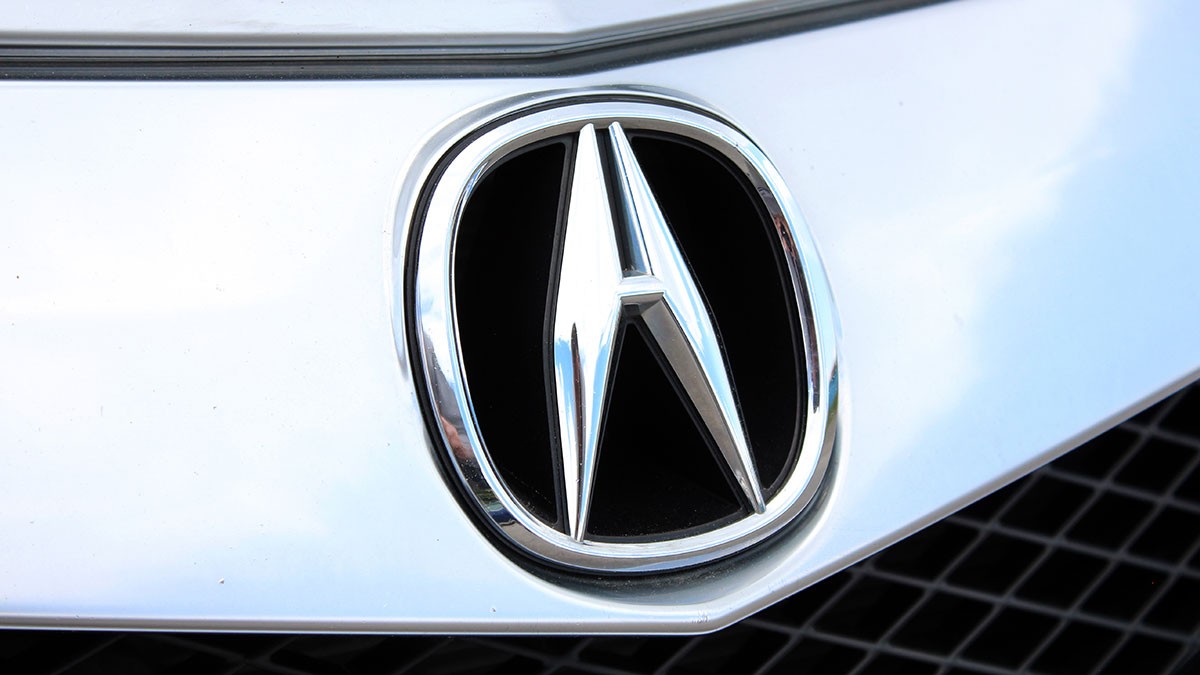 Close-up of an Acura logo on a car grille, featuring a silver emblem with a stylized "A" on a shiny metallic surface.