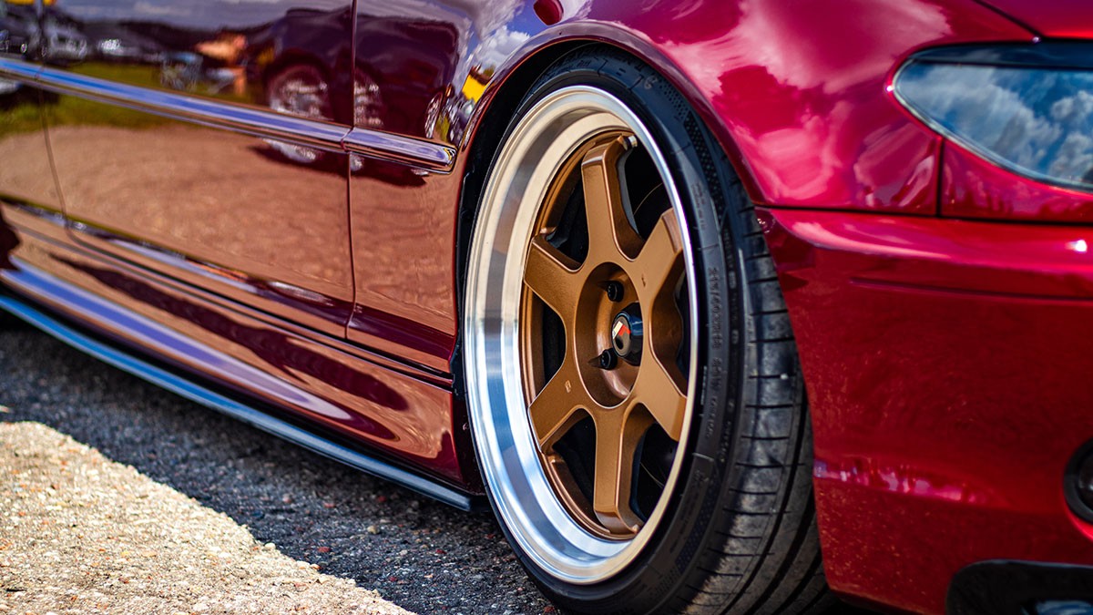 Red sports car with glossy finish, featuring bronze alloy wheels and low-profile tires on a sunny day.