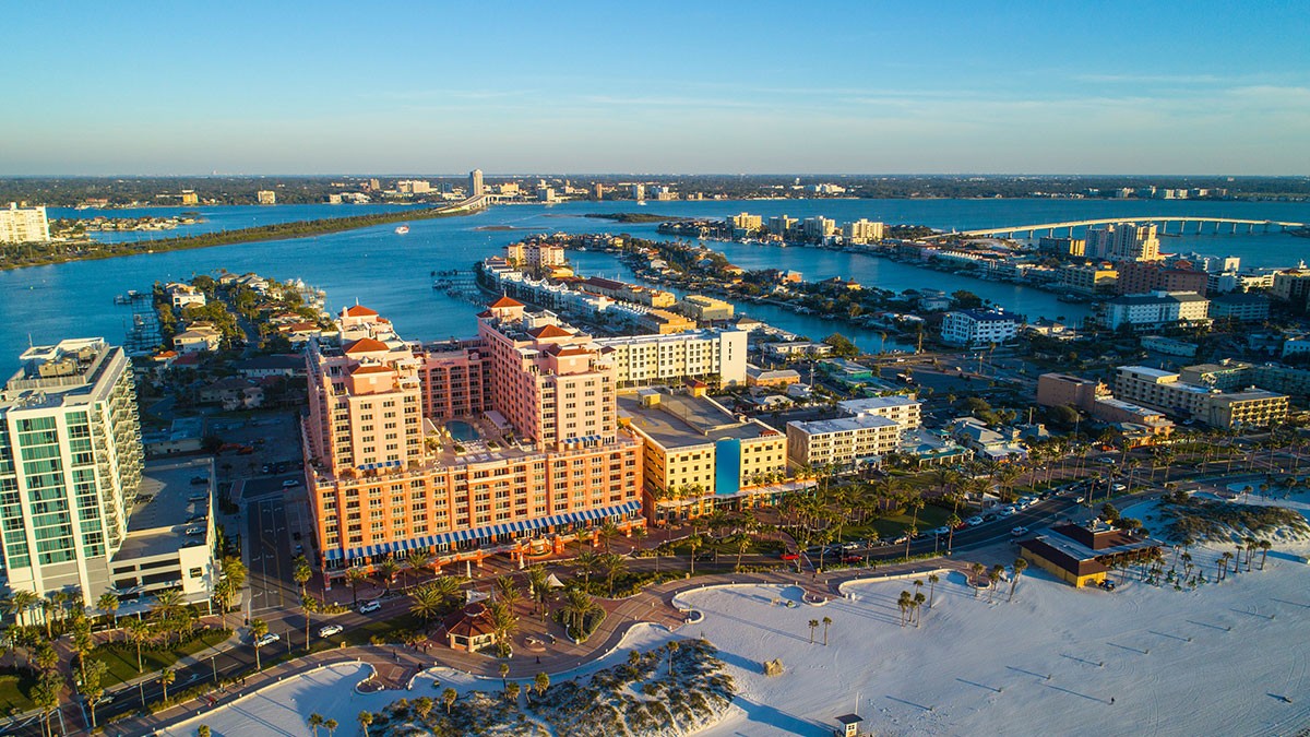 Aerial view of a coastal city with sandy beaches, blue waters, and numerous buildings under a clear sky.