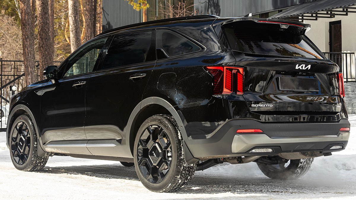 Black SUV parked on a snowy road, featuring modern tail lights and a sleek design, with trees and a building in the background.