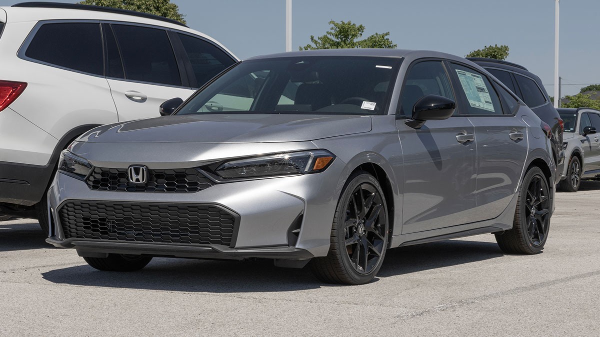 Silver Honda sedan parked in a lot, surrounded by other vehicles, with a bright sky in the background.