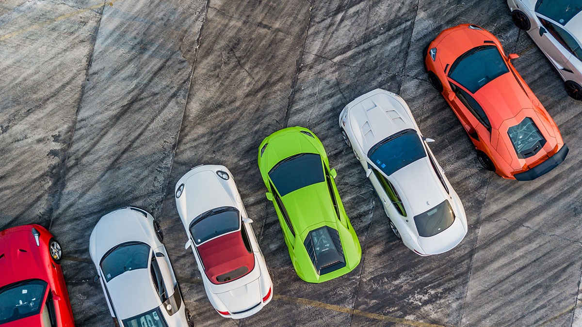 Aerial view of parked sports cars in various colors, including green, orange, and white, on a textured concrete surface.