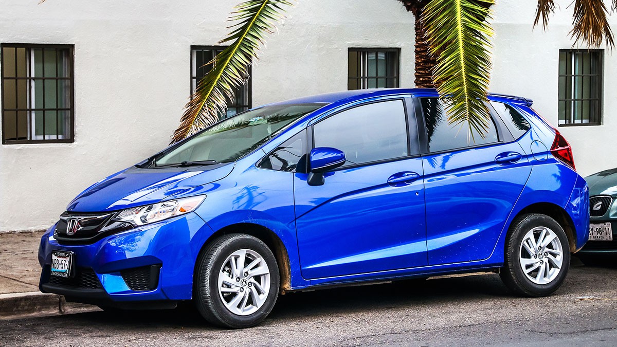 Side profile of a blue Honda Fit parked in a tropical area