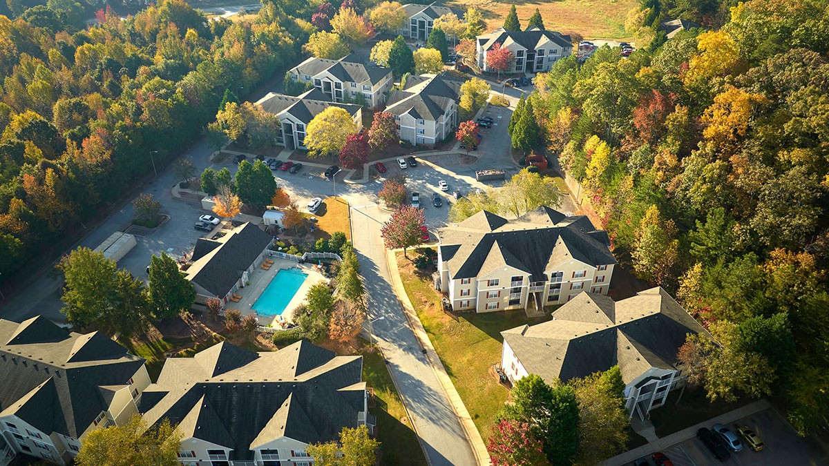 Aerial view of a residential complex with multiple buildings surrounded by trees in fall colors, and a central swimming pool.