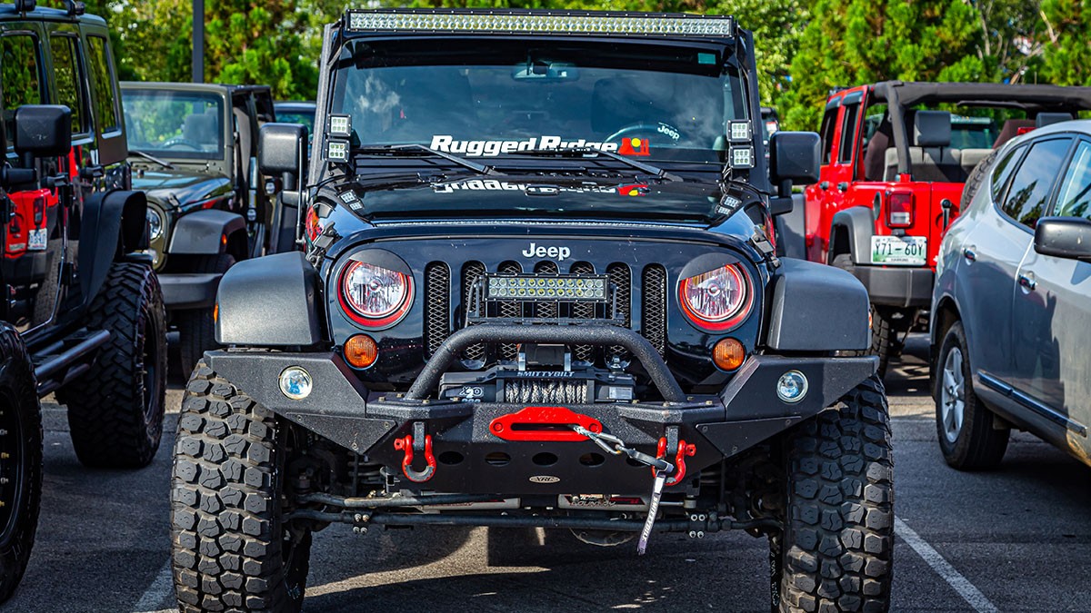Black Jeep Wrangler modified for off-roading, featuring large tires, winch, and bumper, parked in a lot among other vehicles.