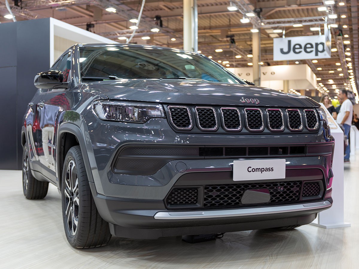 Gray Jeep Compass on display at an indoor auto show, surrounded by bright lighting and signage.