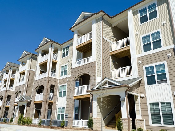Modern apartment building with multiple balconies, beige and white exterior, under a clear blue sky.