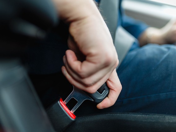 Close-up of a person fastening a seatbelt in a car, focusing on the hand and seatbelt mechanism.