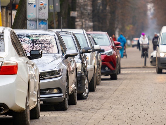Cars parked along a city street, with pedestrians and a cyclist in the background on a cloudy day.