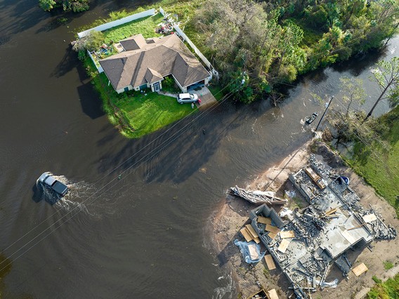 Aerial view of a flooded area with a partially submerged house and car, and a destroyed building surrounded by water and debris.