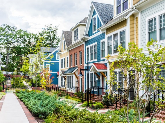 Colorful row houses with varied facades, small front gardens, and a sidewalk, surrounded by greenery on a cloudy day.