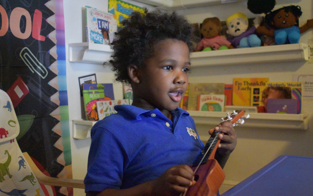 A preschooler singing and playing a ukulele in the classroom