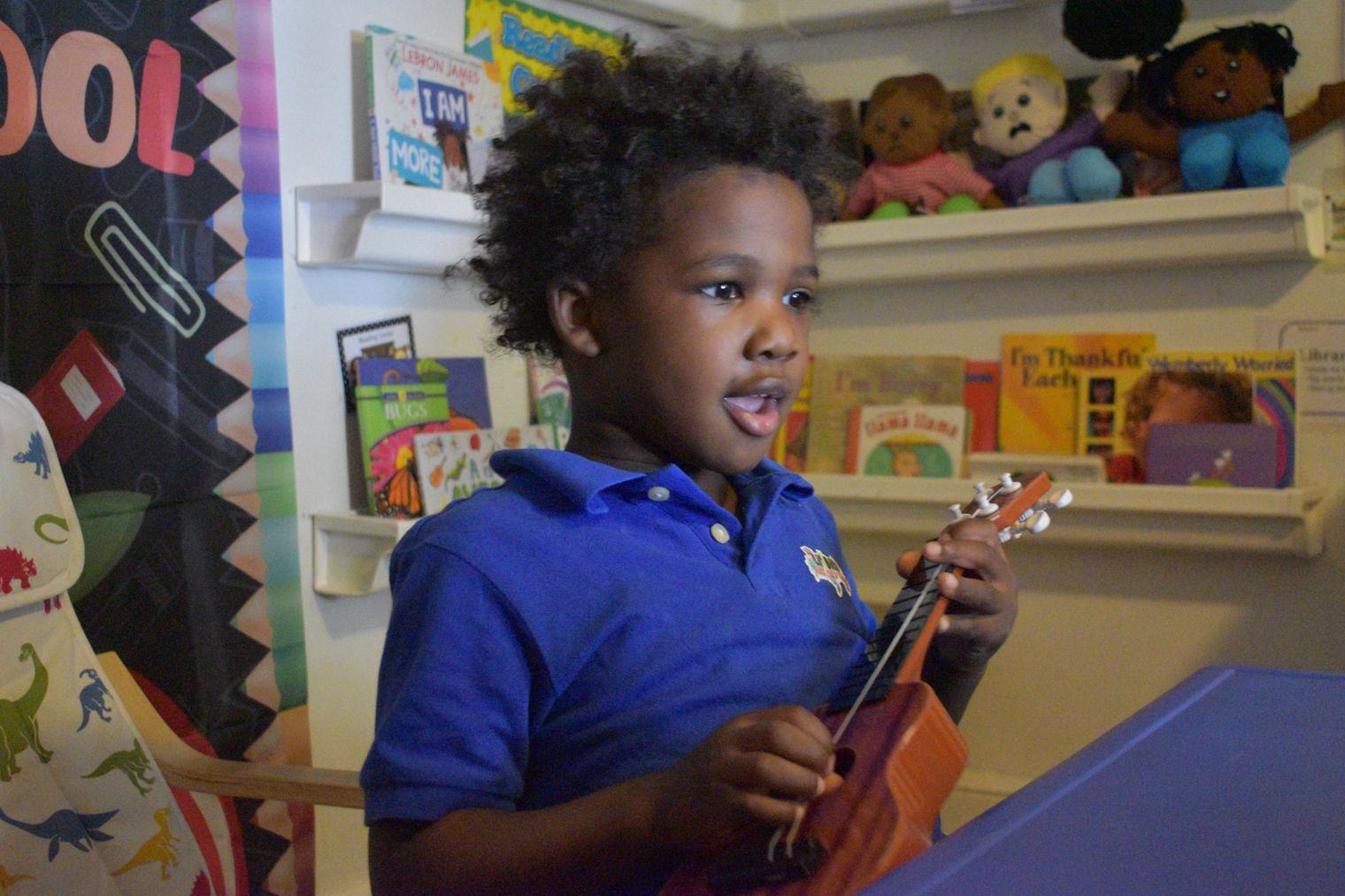 A preschooler singing and playing a ukulele in the classroom